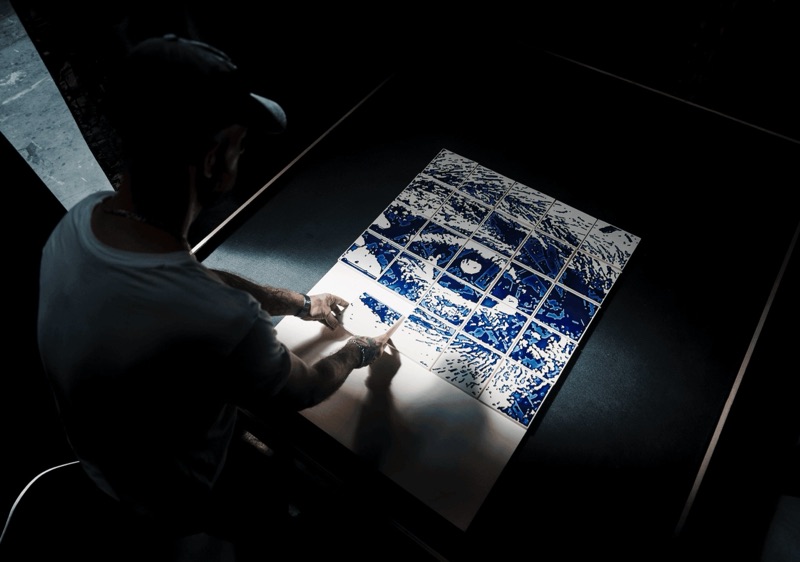 Vhils composing a carved cobalt-glaze tile panel in the Barreiro atelier